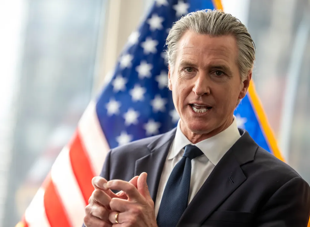 Gavin Newsom, Governor of California, speaks at a press briefing with an American flag in the background.