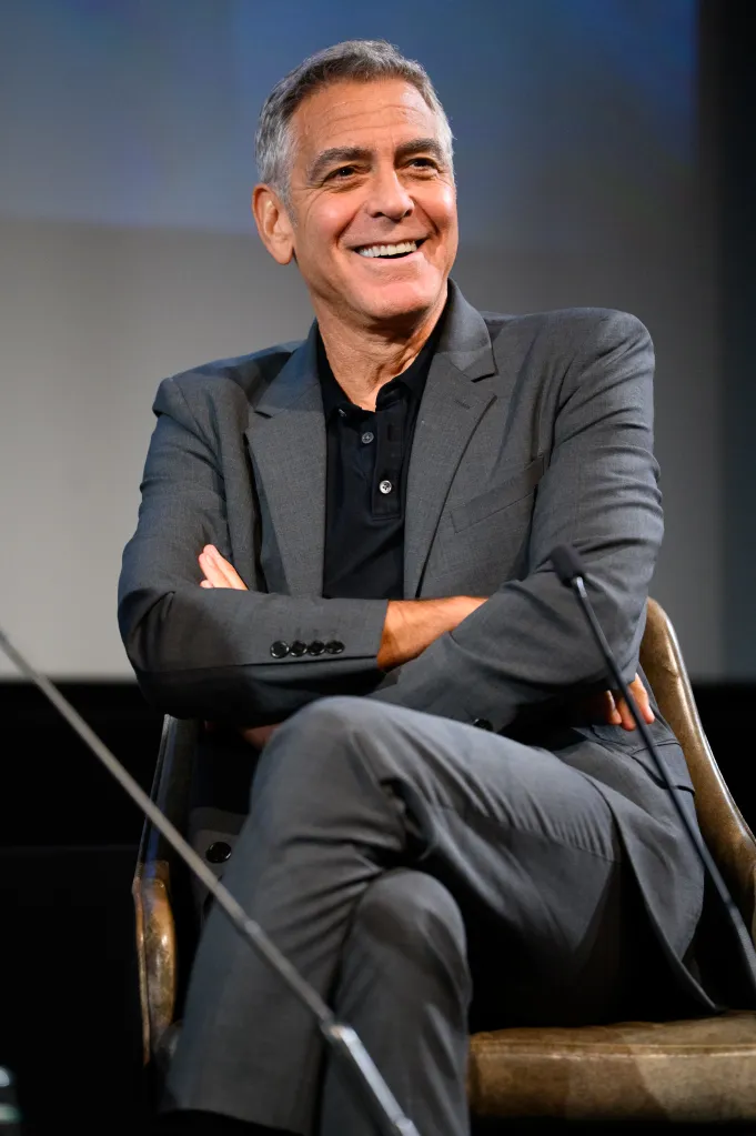 George Clooney smiling while seated with his arms crossed.