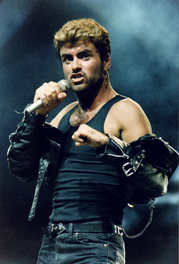George Michael performing on stage in a black tank top and leather jacket.