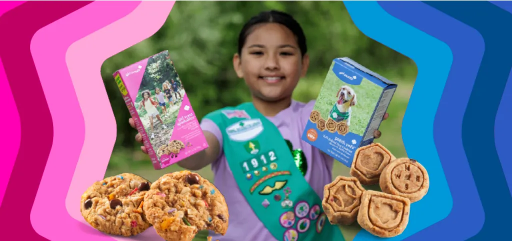 A Girl Scout smiles while holding boxes of the new Girl Scout Sparkables cookie and Patch Pals dog cookie.