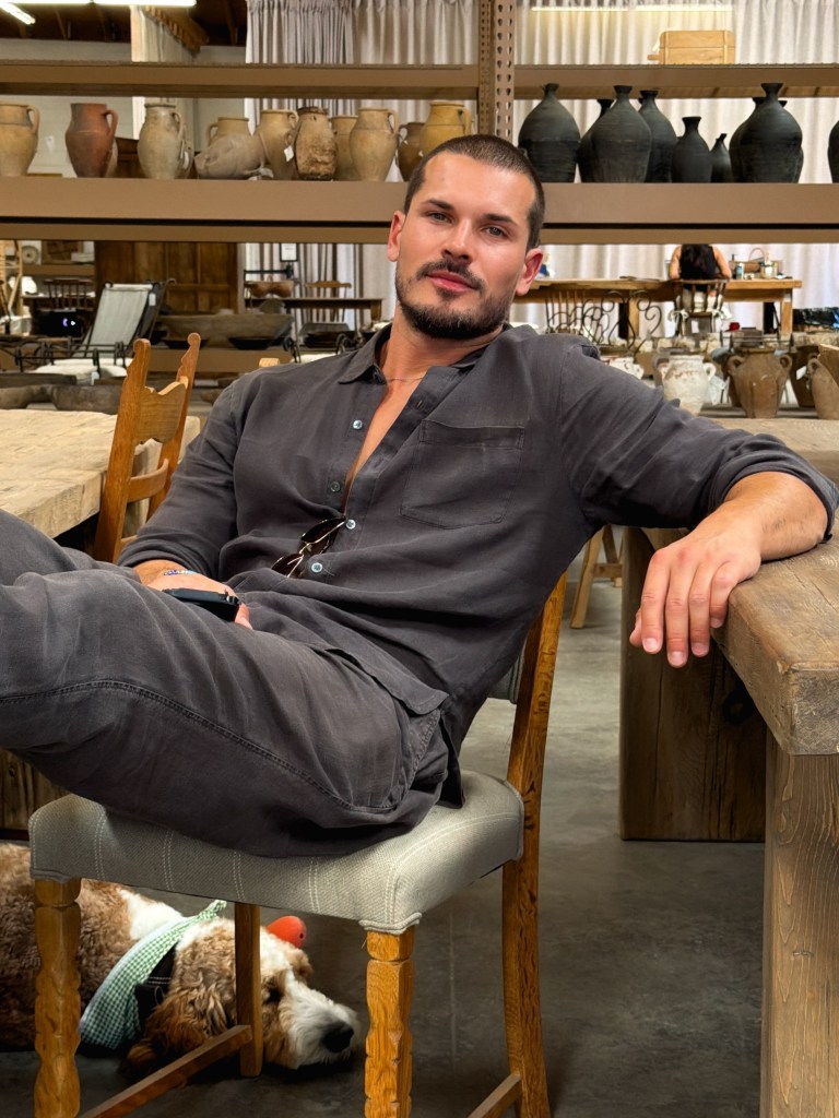 Gleb Savchenko posing in a room filled with pottery, with a dog sleeping under his chair.