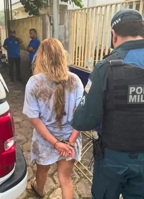 Evelyn Lima Dantas, an influencer suspected of involvement in organized crime, is handcuffed with her back to the viewer while a police officer stands next to her.