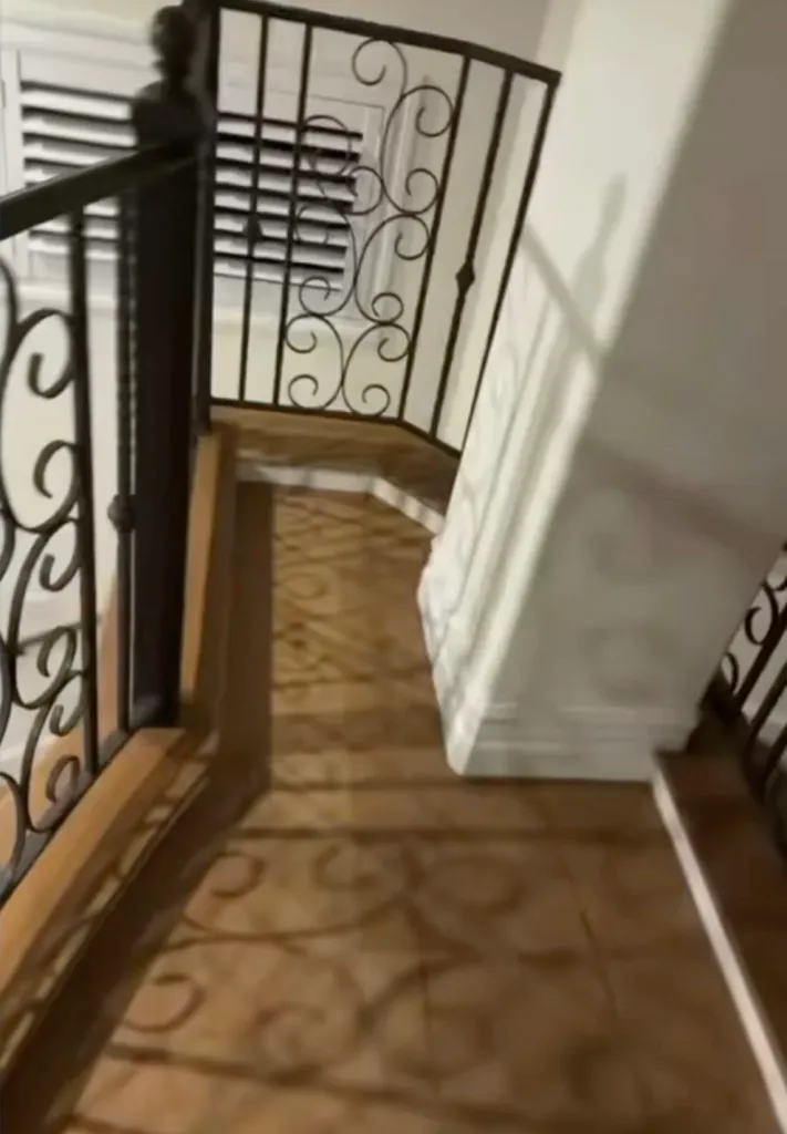 An indoor hallway with wooden flooring, a white pillar, and a black metal railing with scrollwork.