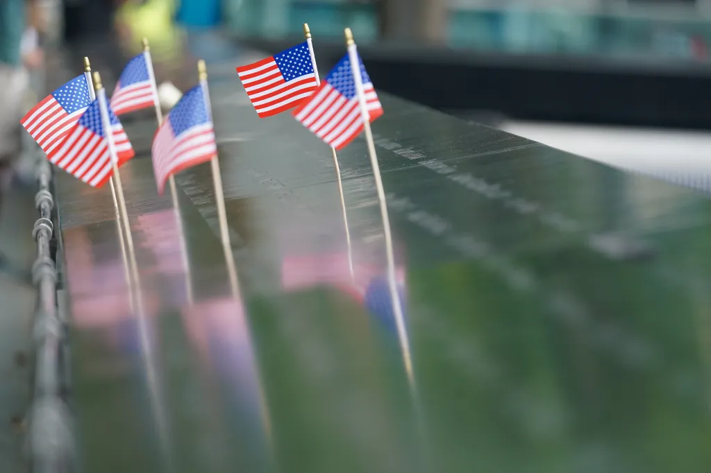 Several American flags are placed along the edge of the 9/11 Memorial.