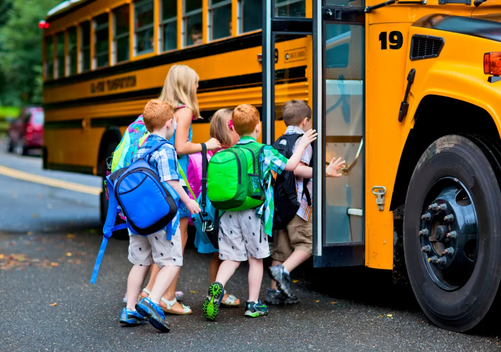 Young children with backpacks board a yellow school bus.