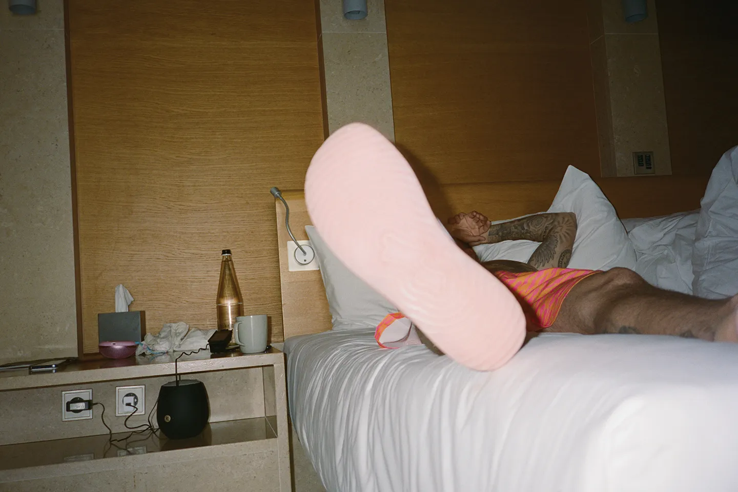 Justin Bieber lying on a bed with a pink flip-flop sole in the foreground.