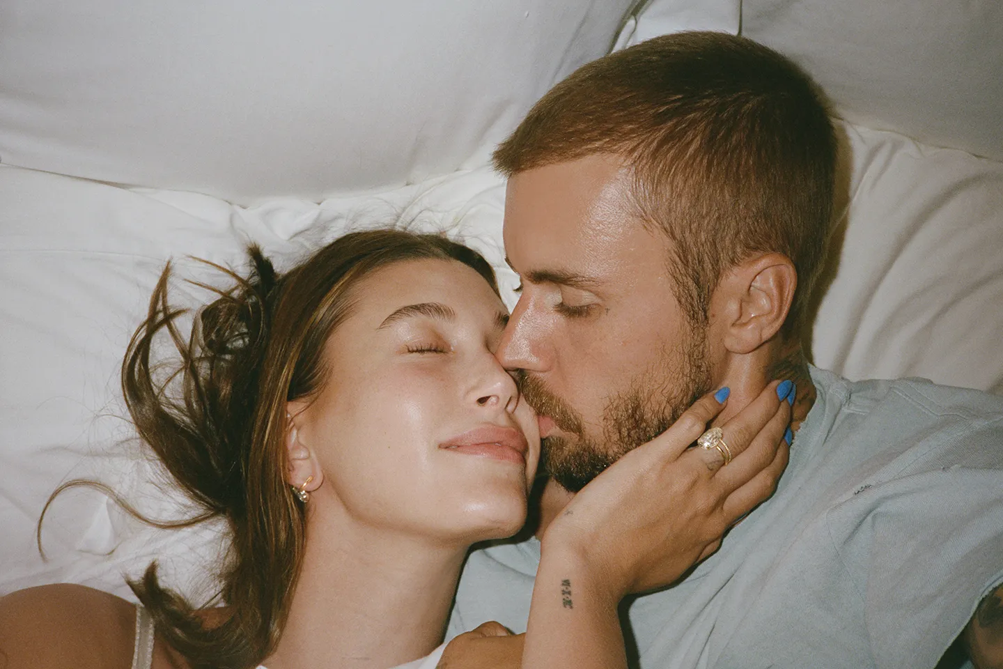 Hailey and Justin Bieber laying together, with Justin kissing Hailey's cheek.