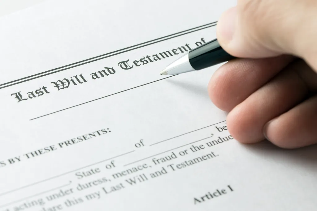 A hand holding a pen over a Last Will and Testament document.