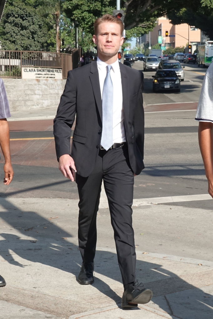 Brian Hickerson in a black suit with a light blue tie walks on a sidewalk in Los Angeles.