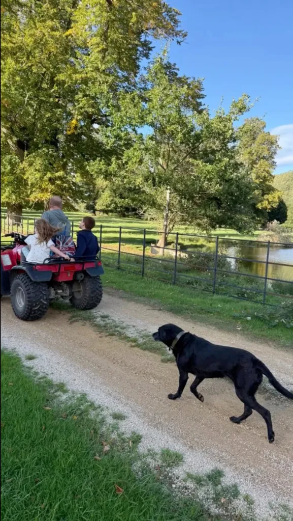 Prince Harry on an ATV with his two children, Prince Archie and Princess Lilibet, with their black labrador Pula walking alongside them.