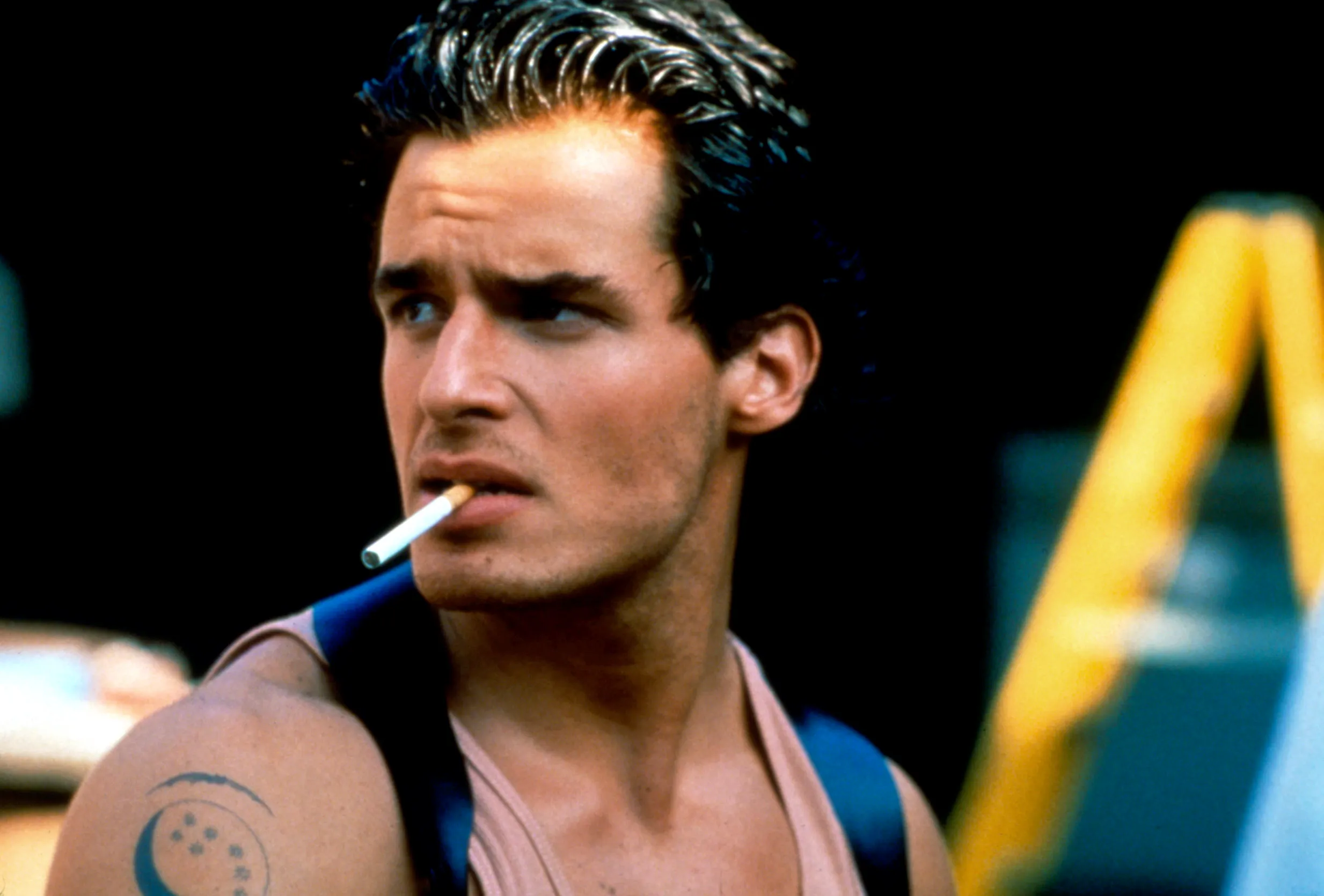 Antonia Sabato Jr. as a young man with a cigarette in his mouth, wearing a tank top, with a crescent moon and stars tattoo on his right shoulder.