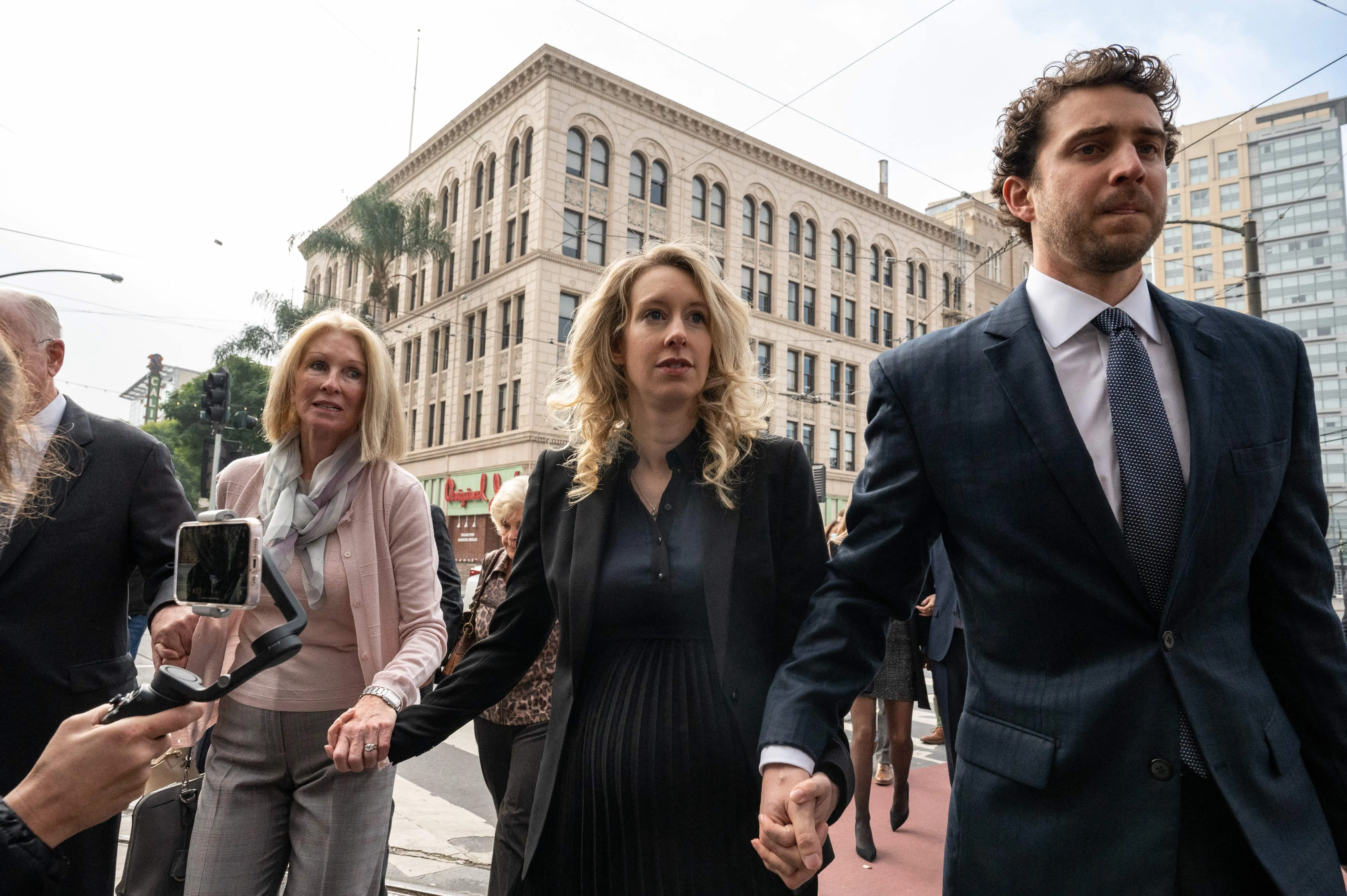 Elizabeth Holmes walking into federal court, holding hands with her mother and partner.