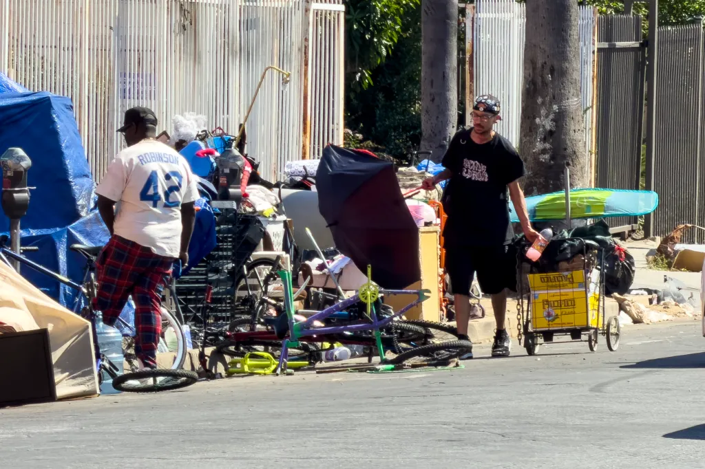 Two unhoused people among their belongings along Olympic Boulevard in downtown Los Angeles.