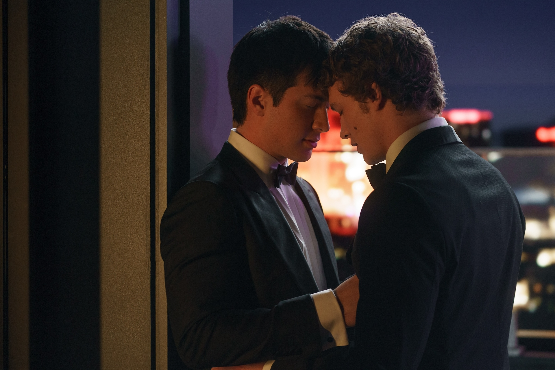 Hudson Williams and Connor Storrie in tuxedos, foreheads touching.