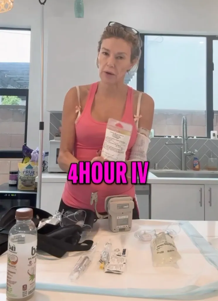 Woman in a pink tank top with an IV drip on her arm, with medical supplies on a table in front of her.