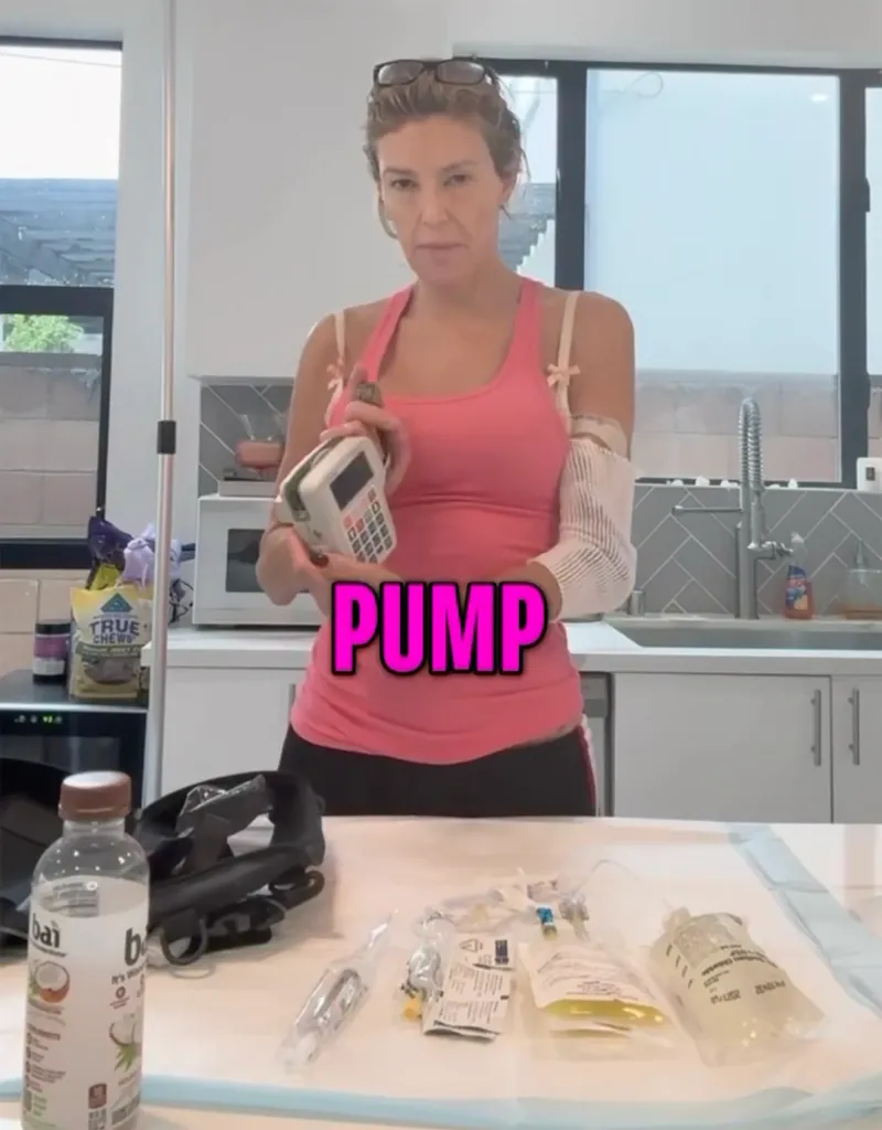 A woman in a pink tank top holds an IV pump and displays various IV supplies on a table.