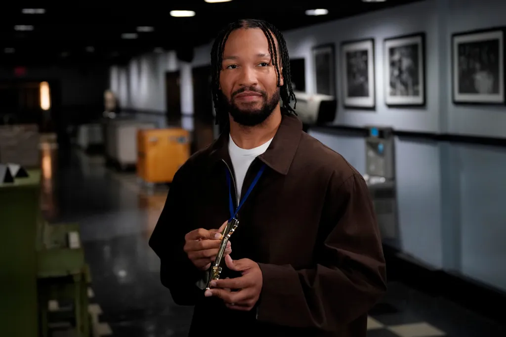 Jalen Brunson in a brown jacket, holding a golden key on a blue lanyard for Saturday Night Live promos.