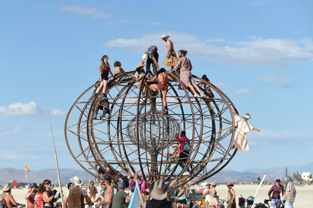 People climbing on a large metal globe art installation at Burning Man in Black Rock Desert.