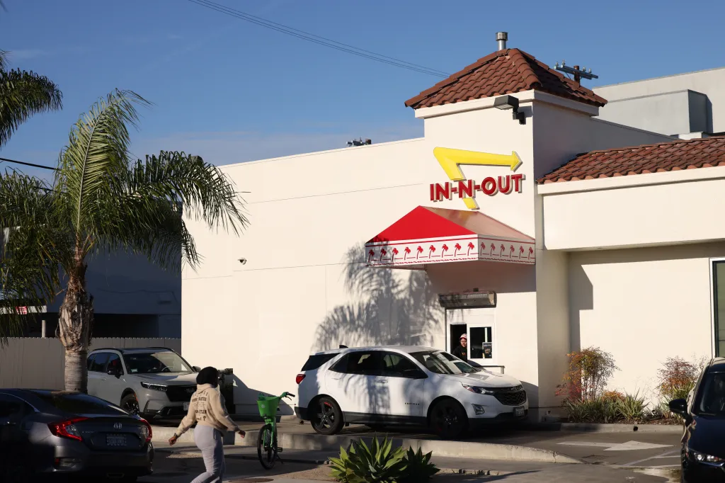 In-N-Out Burger restaurant in Culver City, California, with a palm tree, cars in a drive-thru, and a person walking by a green bicycle.
