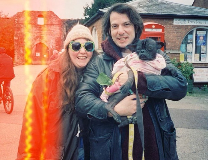 Lena Dunham and Attawalpa smiling with a pug in a sling.