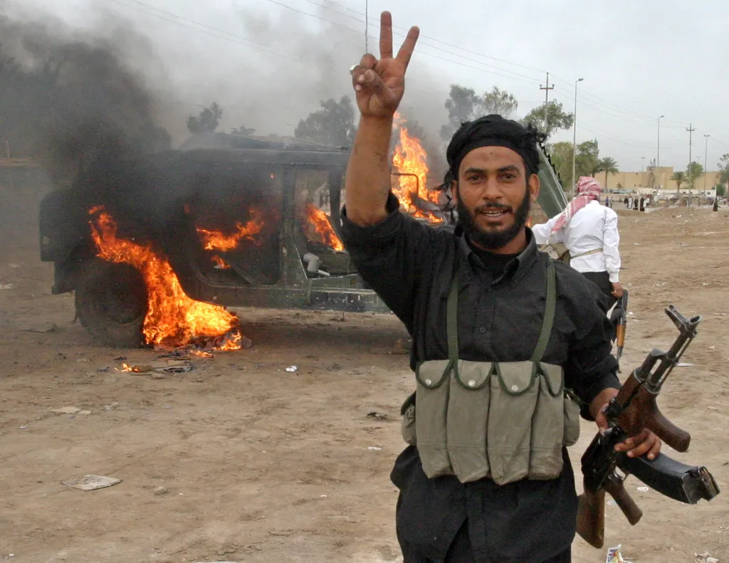 An Iraqi militiaman from Shi'ite cleric Moqtada al-Sadr's Mehdi Army gestures near a burning US Army Humvee vehicle, which was captured during a morning gun battle and later set alight, in Kufa, Iraq, Sept. 30, 2026.