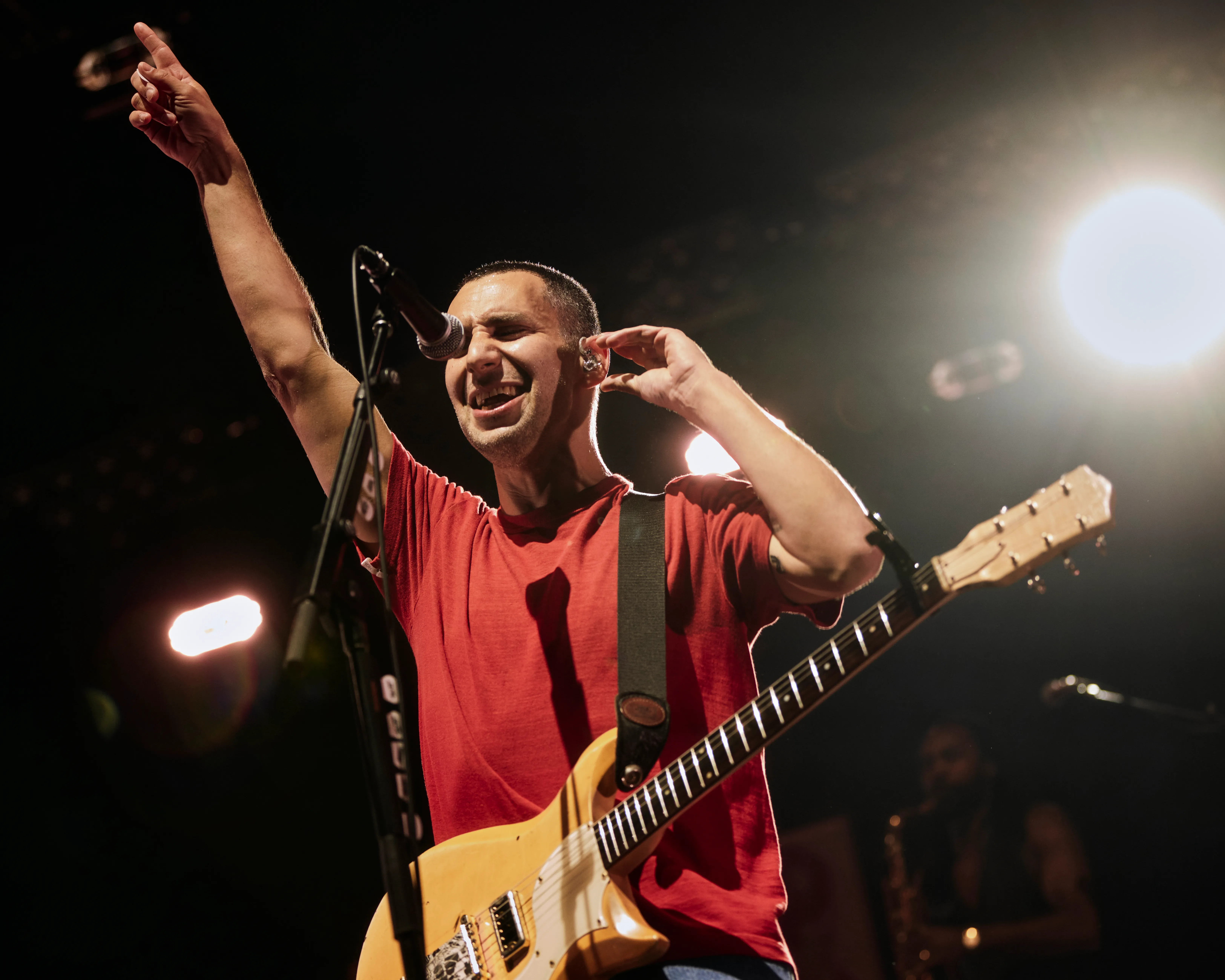 Jack Antonoff of Bleachers performing onstage, holding a guitar and pointing his left hand upwards.