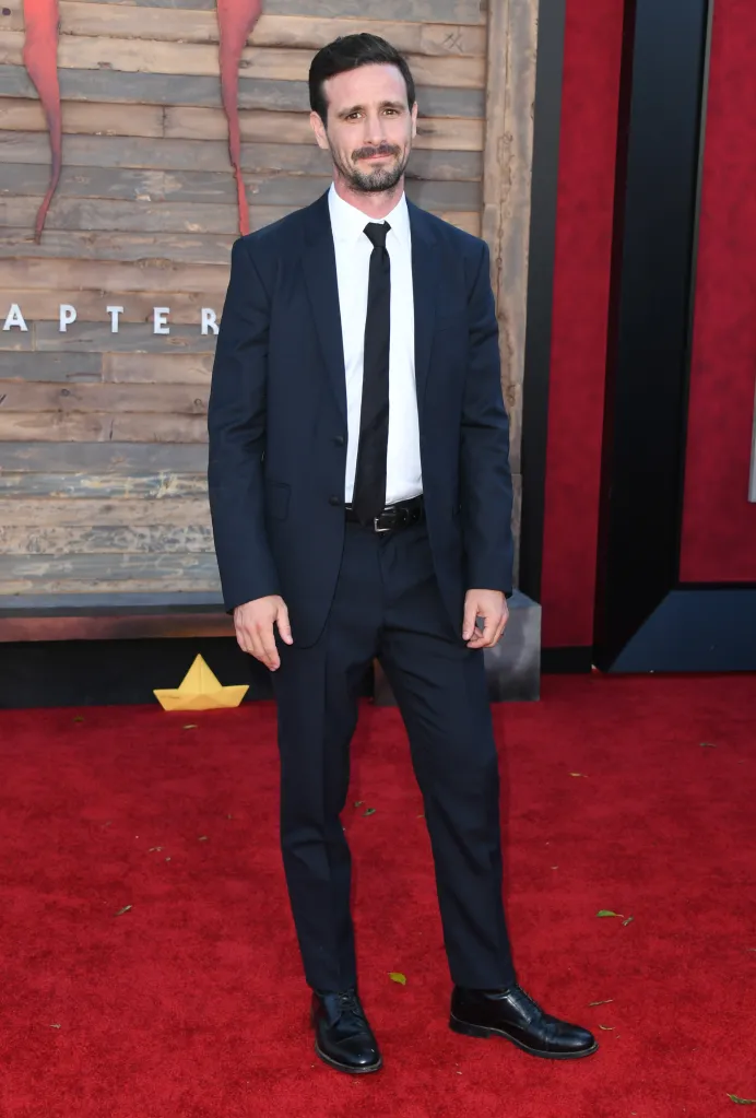 James Ransone poses on a red carpet in a dark suit and tie.
