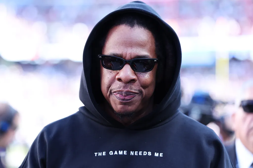 Jay-Z wearing sunglasses and a black hoodie with the words 