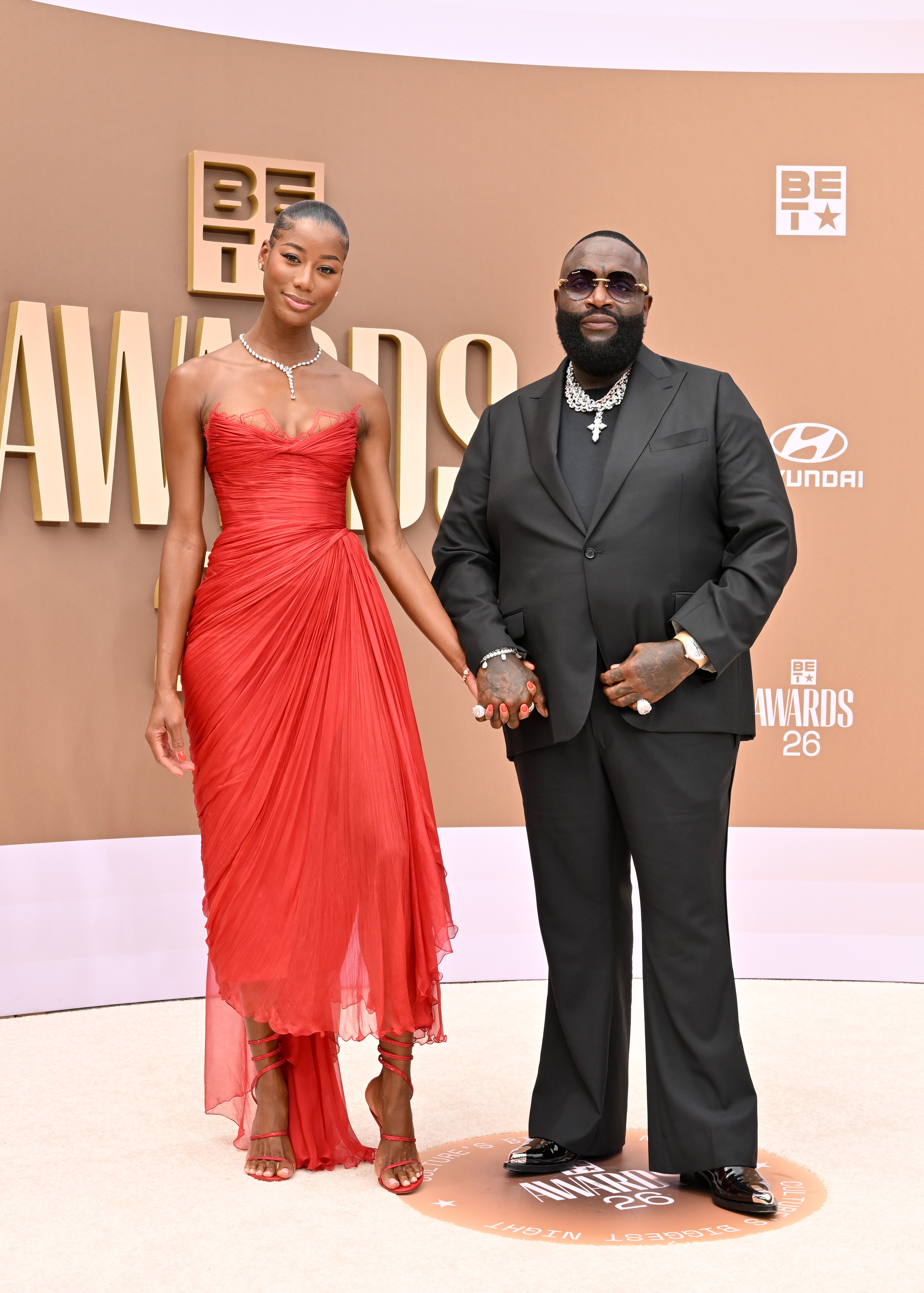 Jazzma Kendrick in a red gown and Rick Ross in a black suit pose at the BET Awards.