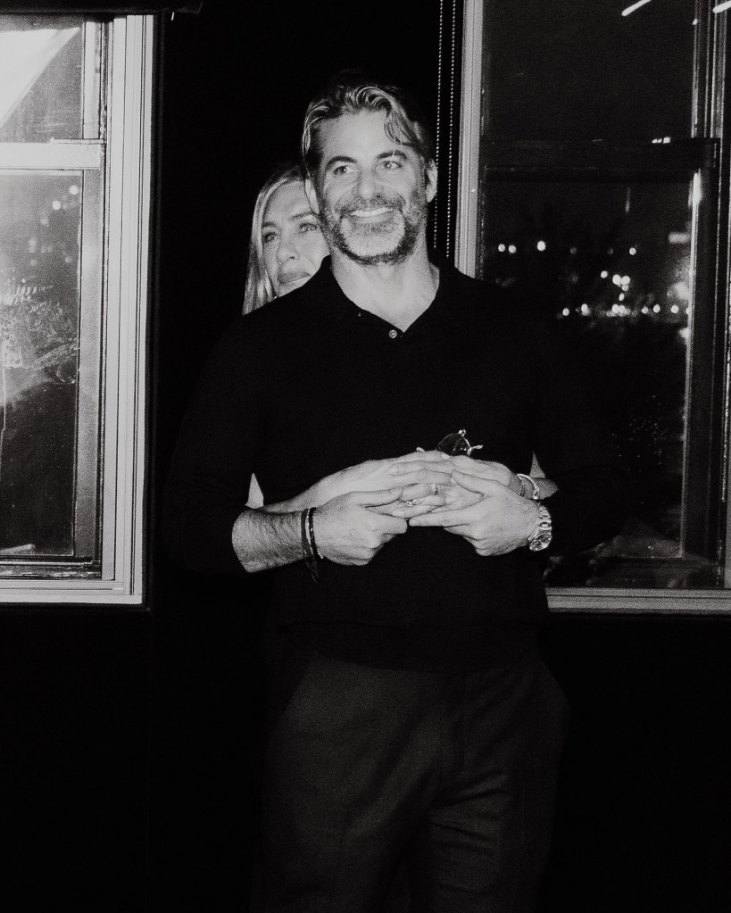 Jennifer Aniston embracing Jim Curtis from behind as they stand by a window.