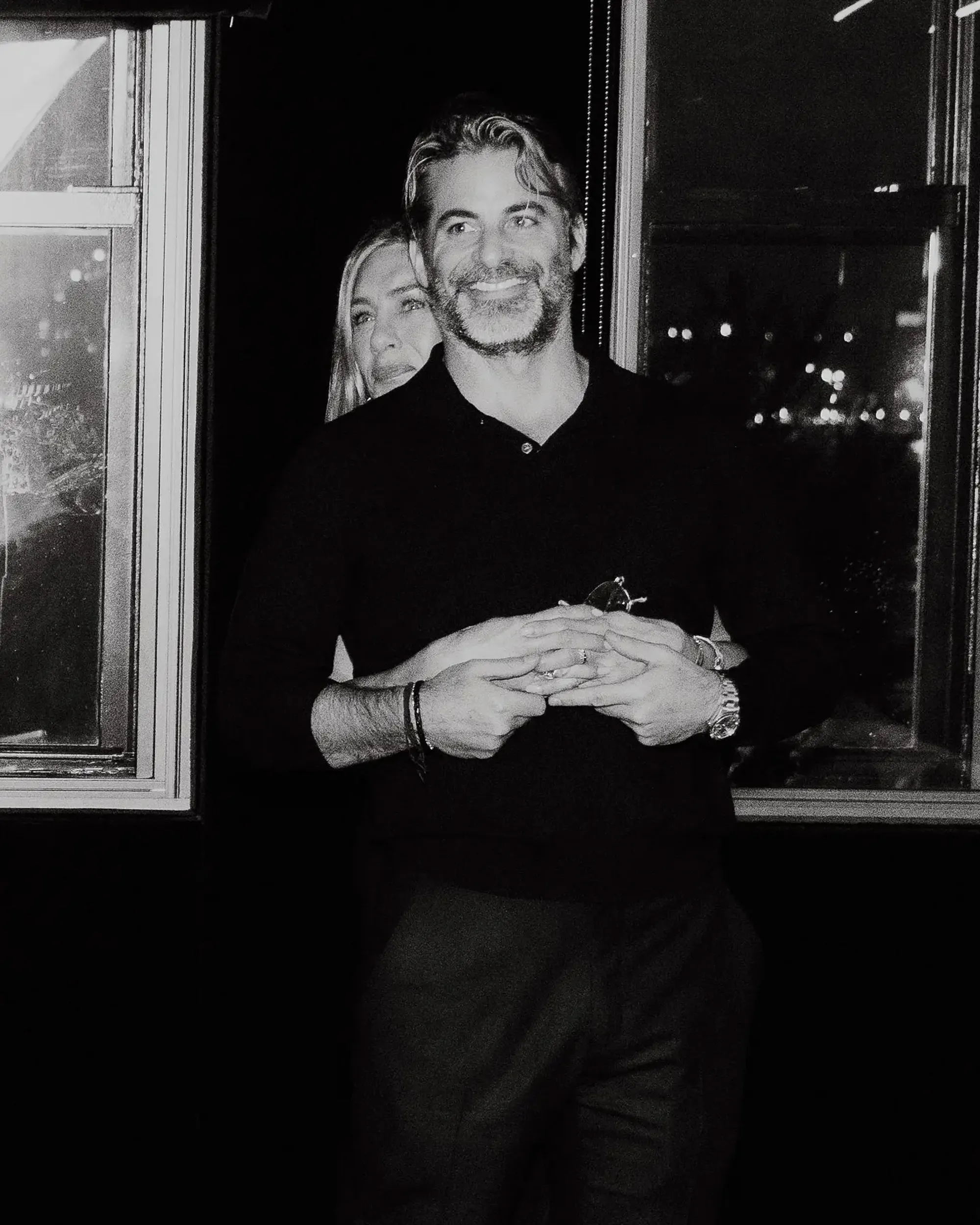Jennifer Aniston embracing Jim Curtis from behind, holding hands.