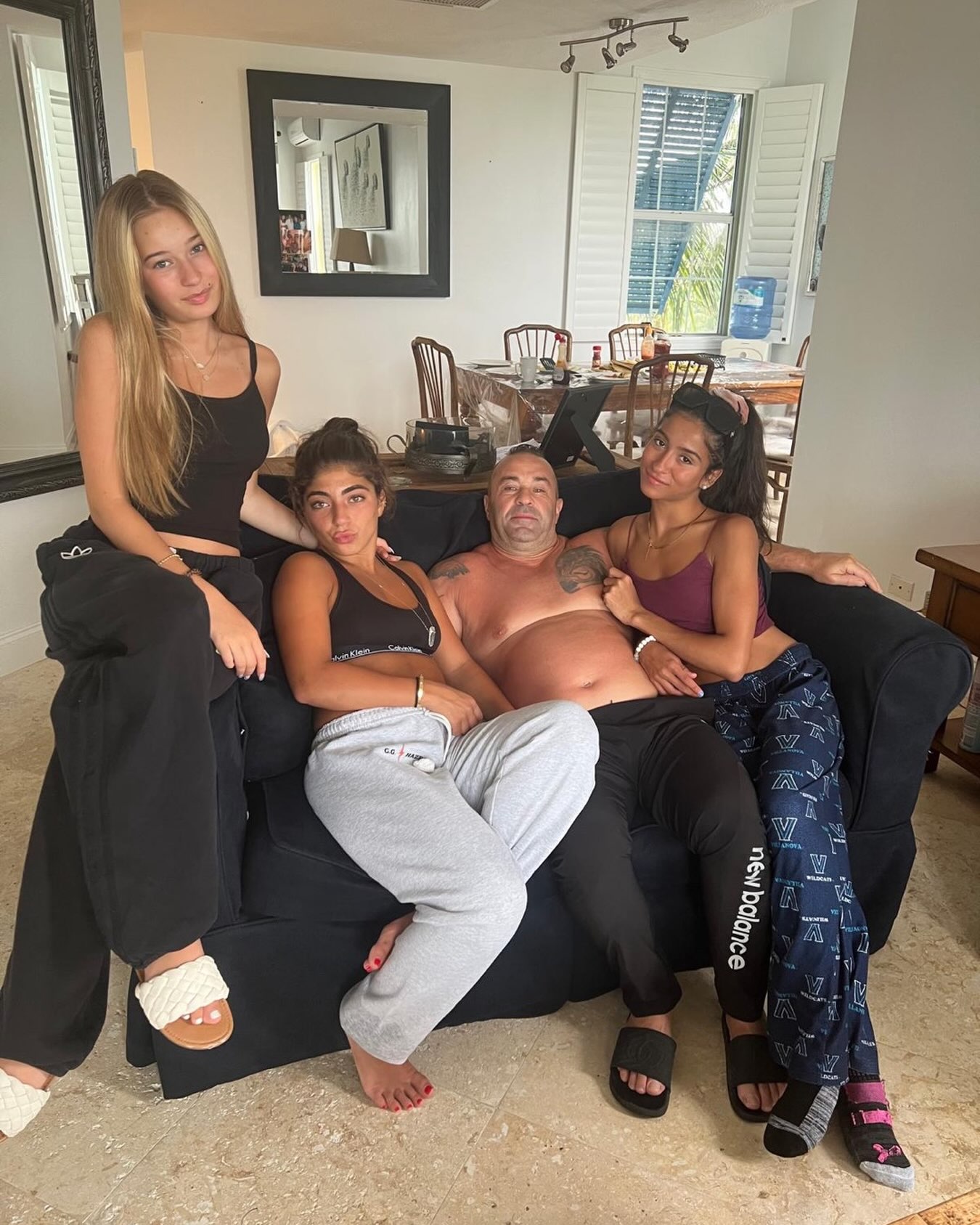 Joe Giudice and his three daughters posing together on a couch.