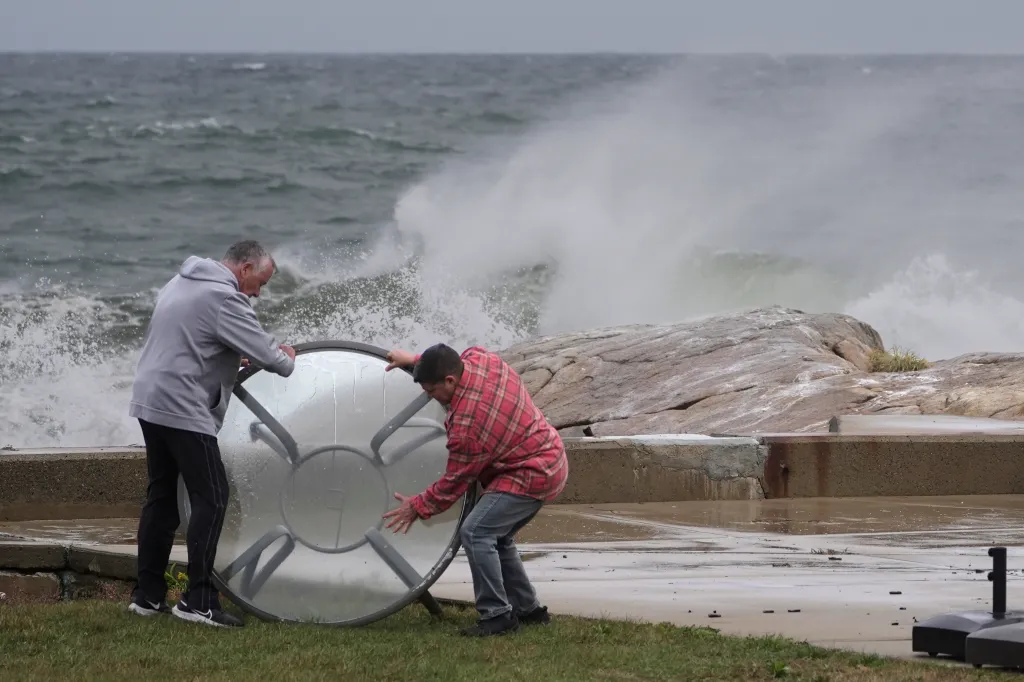 People move a outdoor table away from the shorefront during preparations for the storm in Gloucester, Mass.