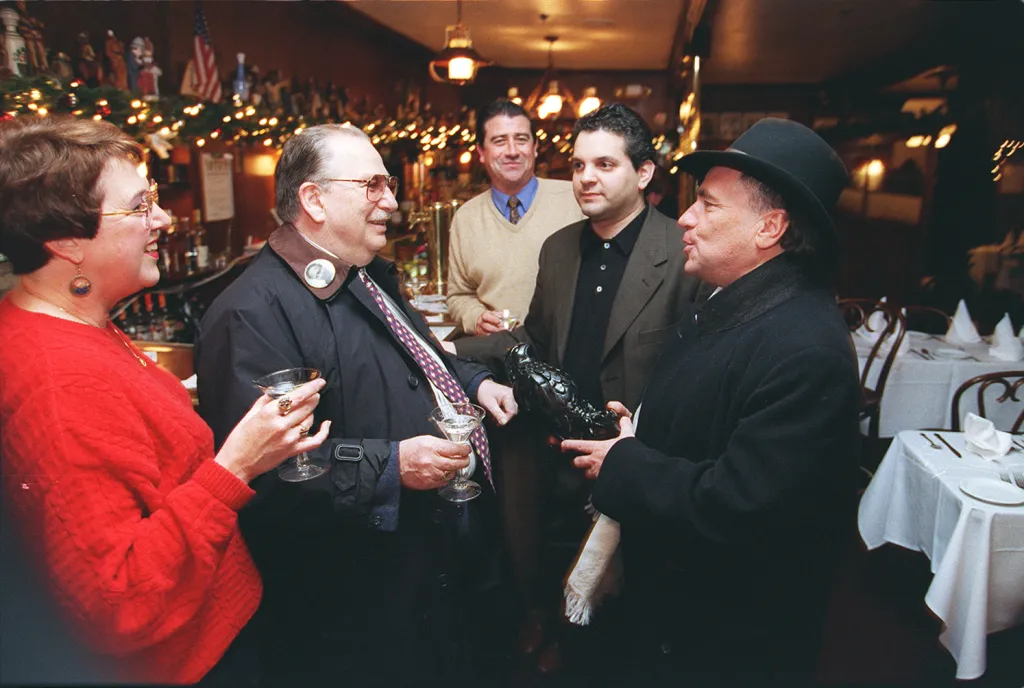 Group of five people gathered at John's Grill with one man holding a 