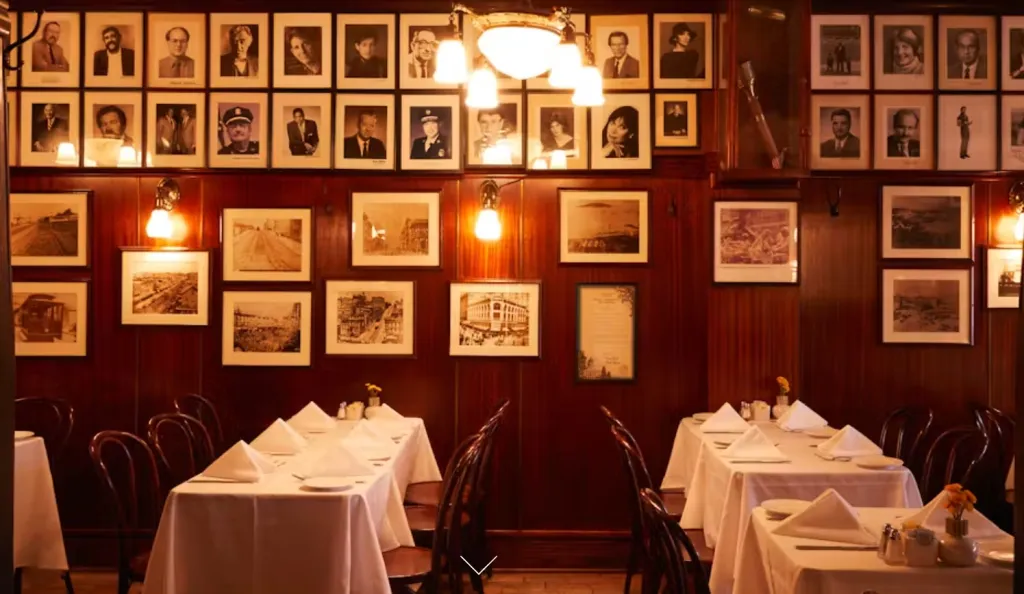Dining area with wood paneled walls covered with framed portraits and historical photos, and tables set with white tablecloths.