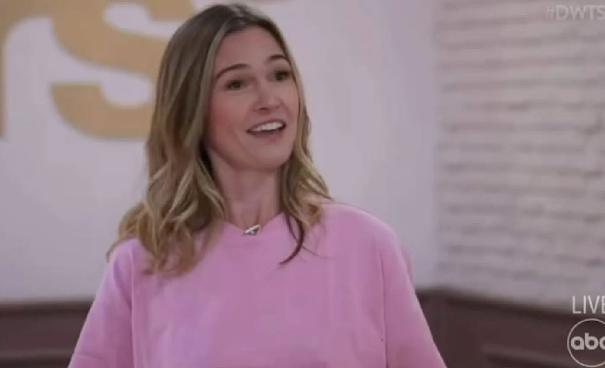 Julia Stiles in a pink top, smiling at the camera, with the #DWTS logo visible.