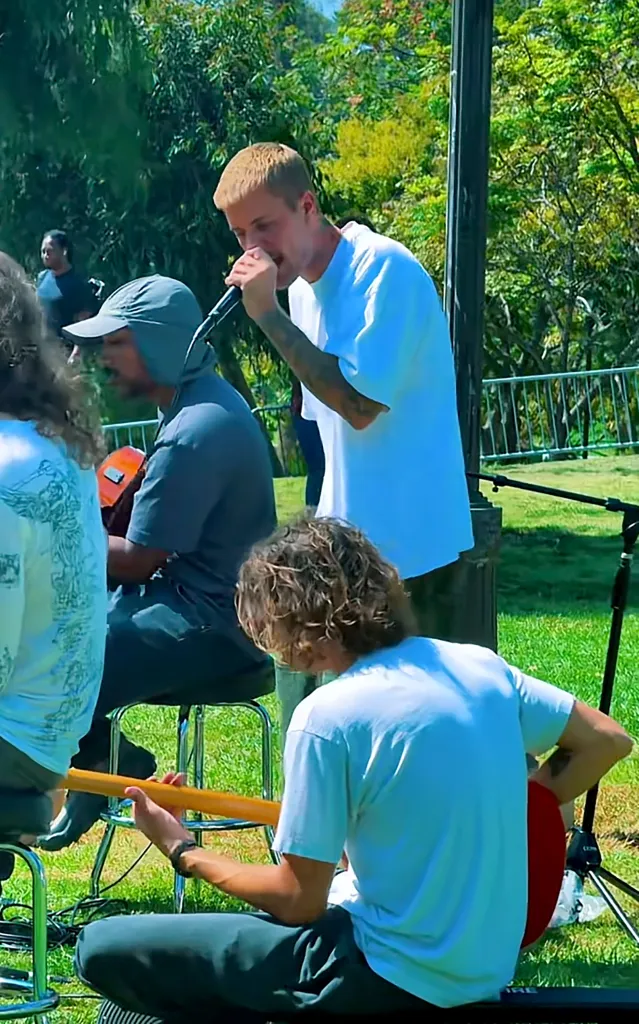 Justin Bieber singing into a microphone outdoors in MacArthur Park, surrounded by other musicians.