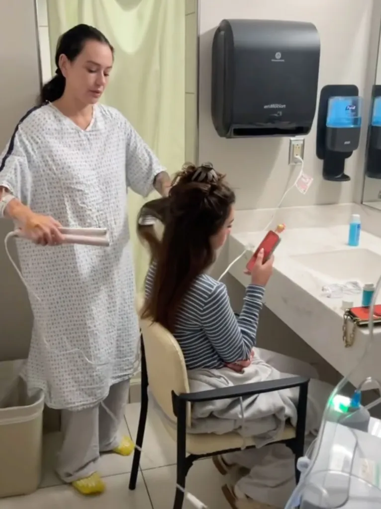 Jenni Farley (JWoww) uses a flat iron to style a seated person's hair in a hospital bathroom.