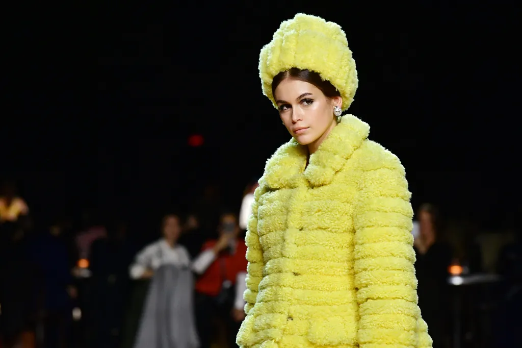 Kaia Gerber on the runway at the Marc Jacobs Fall 2020 show, wearing a bright yellow, textured coat and matching hat.