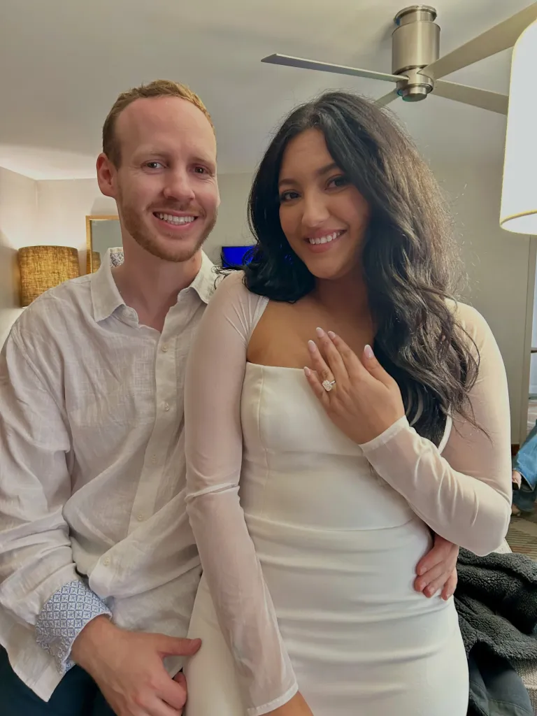 Kailauna Viola Mills poses with a man, with her left hand resting on her chest, showing an engagement ring.