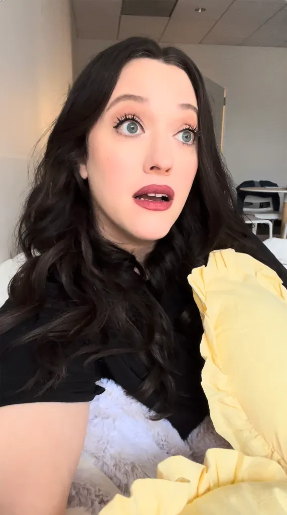 Kat Dennings looking surprised with her mouth slightly open and eyes wide, holding a yellow object.