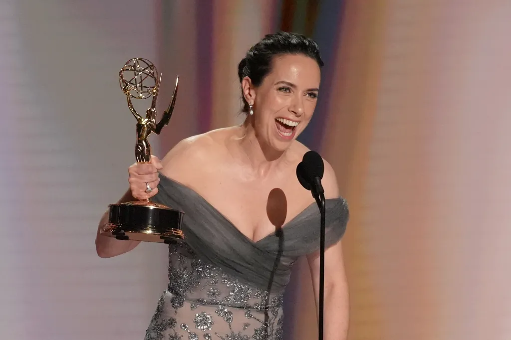 Kate O'Flynn holding her Emmy Award and laughing into a microphone.