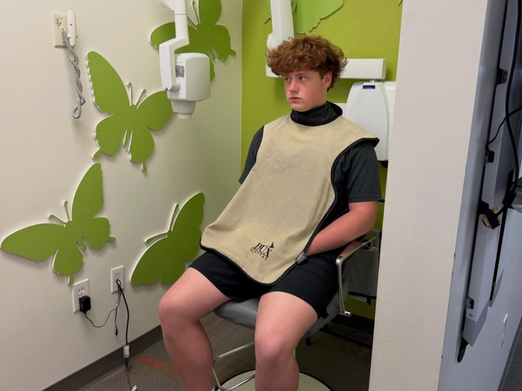 Kim Zolciak-Biermann's son, KJ Biermann, wearing a protective dental apron while seated in a dental office.