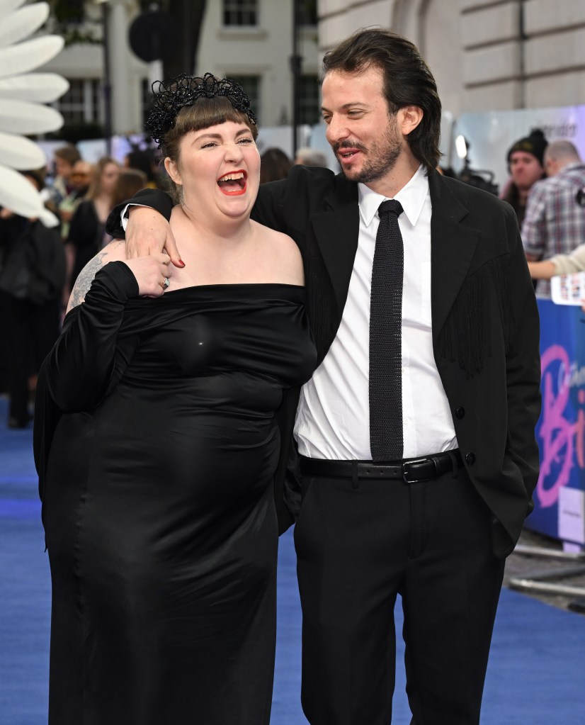Director Lena Dunham laughs alongside Luis Felber on a blue carpet.