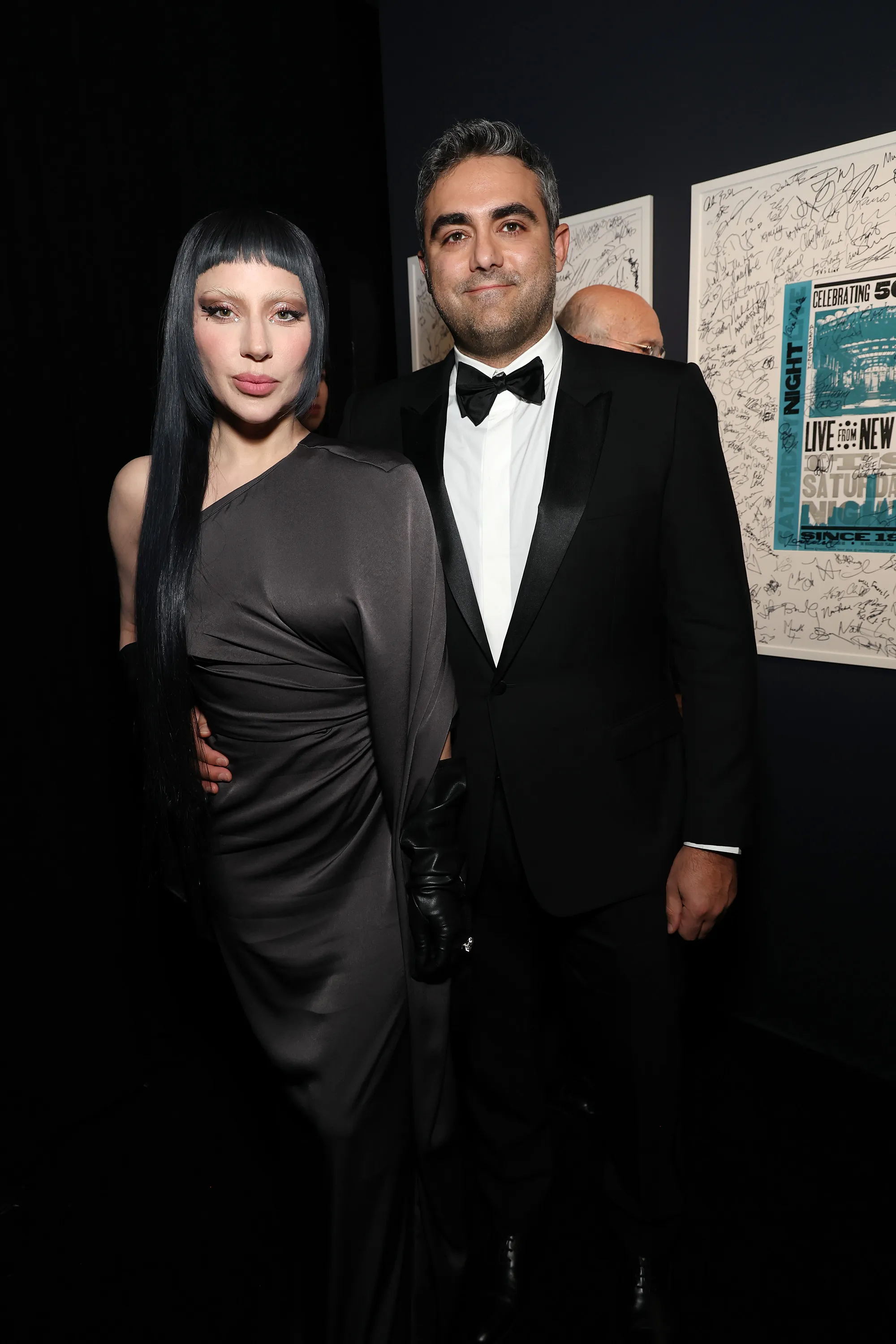 Lady Gaga in a dark grey gown and Michael Polansky in a black tuxedo on the red carpet.