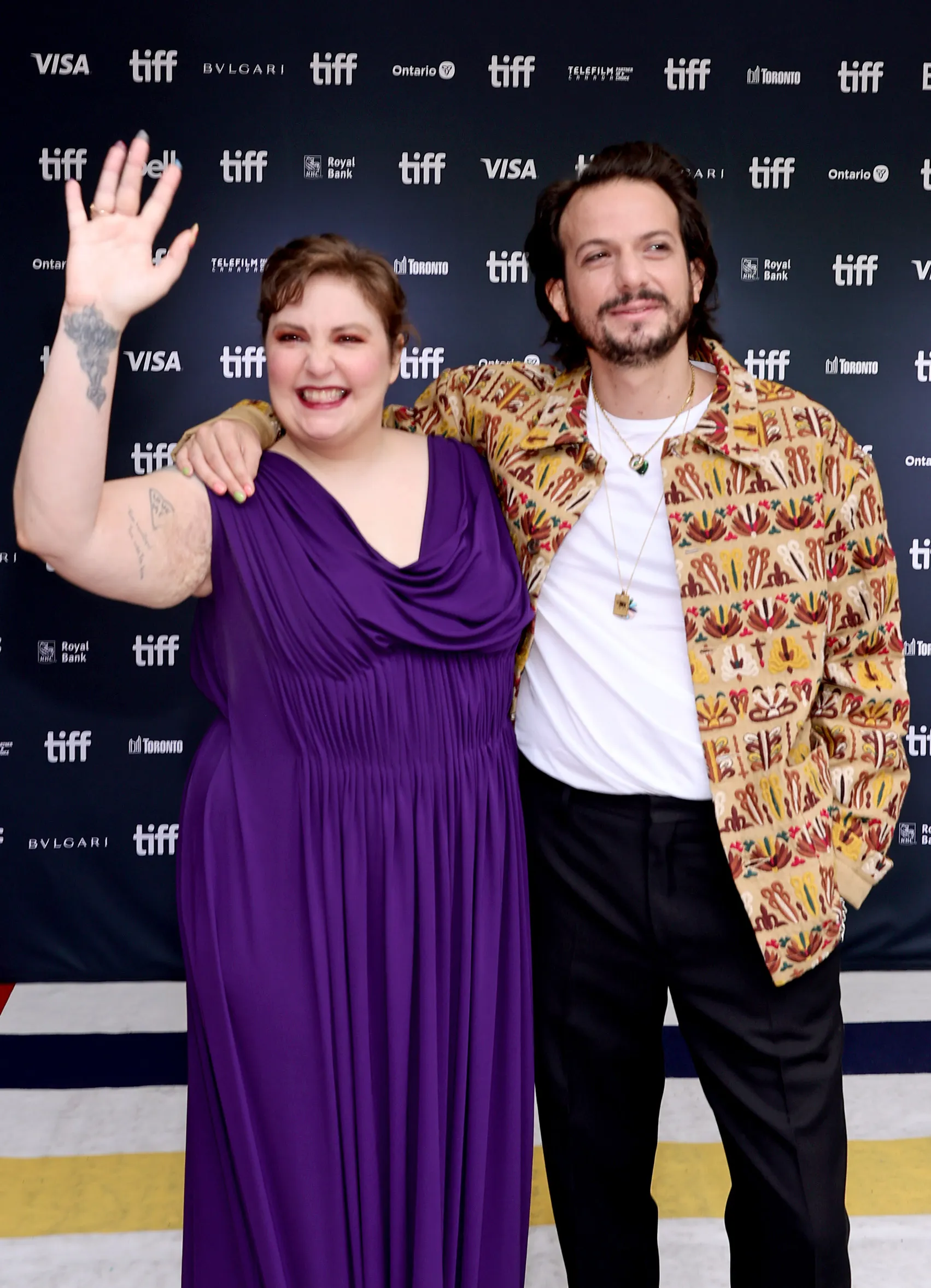 Lena Dunham in a purple dress and Luis Felber in a patterned jacket attend the 
