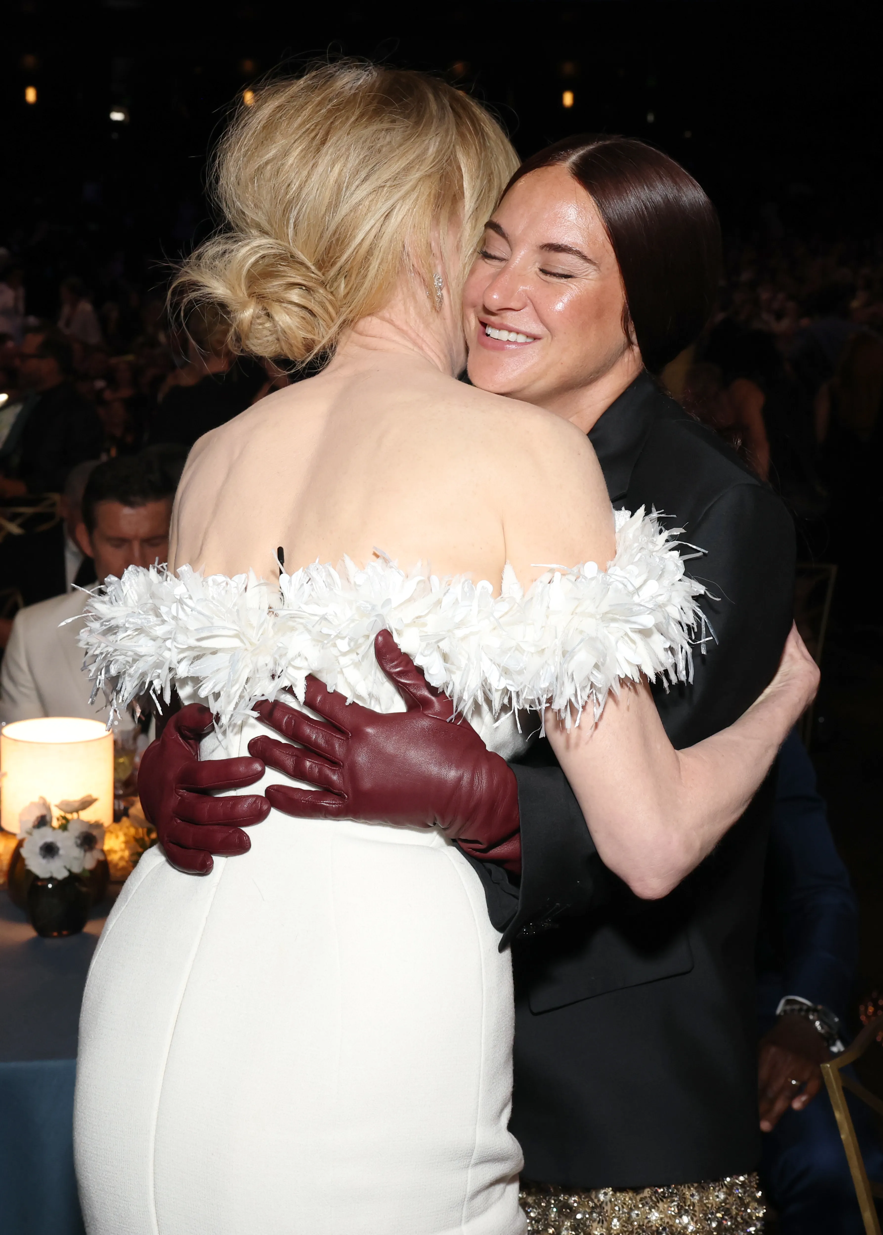 Nicole Kidman, in an off-white feather-trimmed gown and burgundy gloves, hugs Shailene Woodley, in a black jacket and sequined skirt, at the 78th Primetime Emmy Awards.