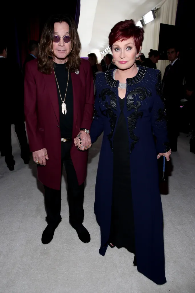 Ozzy and Sharon Osbourne holding hands, standing on a white carpet.