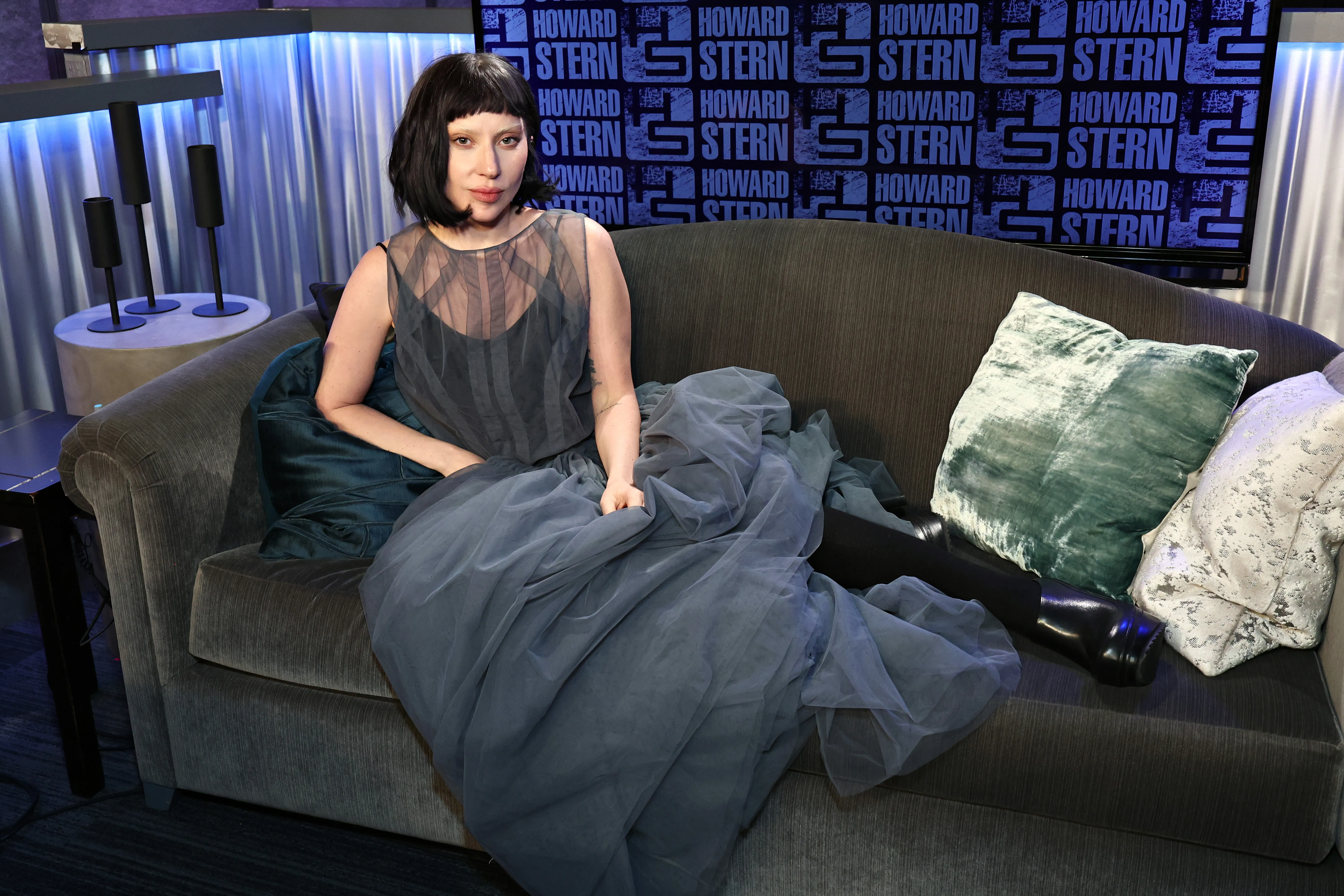 Lady Gaga sitting on a couch in a sheer gray gown at SiriusXM's 'The Howard Stern Show'.