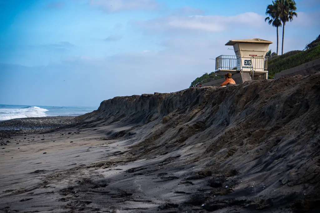 Erosion at Tamarack State Beach in Carlsbad, California with a lifeguard tower and palm trees in the background.